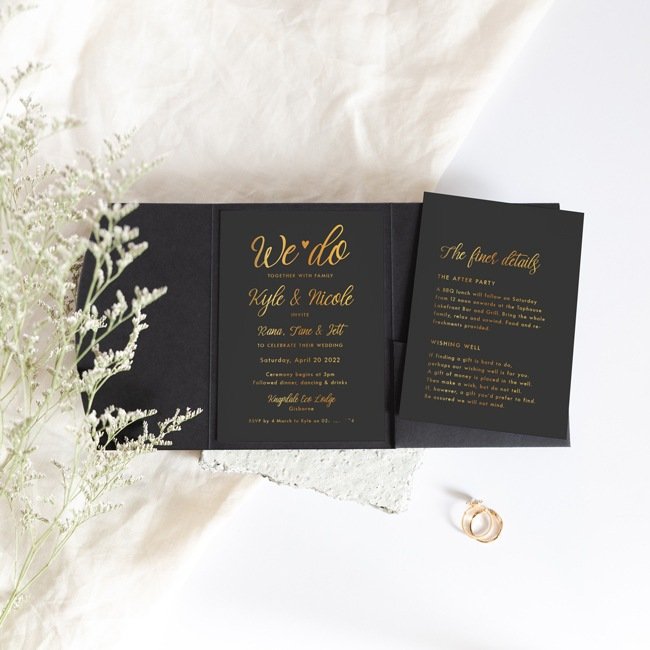 black and gold pocketfold wedding invitation with flowers in foreground